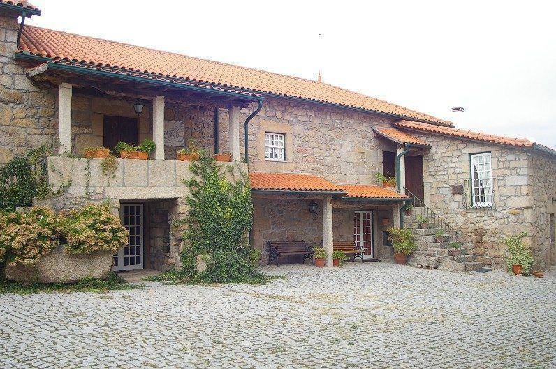 Casa de pedra com telhado de telha cerâmica, pórtico e pátio pavimentado em calçada portuguesa